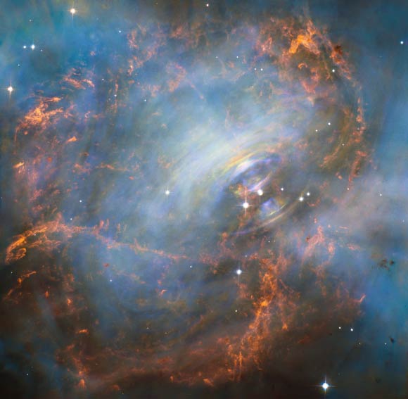 En regardant au cœur de la nébuleuse du Crabe, cette image Hubble révèle le cœur battant de l'un des vestiges les plus historiques et les plus étudiés d'une supernova, une étoile en explosion. L'étoile à neutrons qui se trouve au centre de la nébuleuse a à peu près la même masse que le Soleil, mais elle est comprimée en une sphère incroyablement dense qui ne fait que quelques kilomètres de diamètre. Tournant 30 fois par seconde, l'étoile à neutrons émet des faisceaux d'énergie détectables qui donnent l'impression qu'elle est pulsée. Le cliché de Hubble est centré sur la région entourant l'étoile à neutrons (la plus à droite des deux étoiles brillantes près du centre de cette image) et les débris filamenteux en expansion et en lambeaux qui l'entourent. La vue précise de Hubble permet de saisir les détails complexes du gaz incandescent, représenté en rouge, qui forme un mélange tourbillonnant de cavités et de filaments. À l'intérieur de cette coquille se trouve une lueur bleue fantomatique qui est le rayonnement émis par les électrons qui tournent en spirale à une vitesse proche de celle de la lumière dans le puissant champ magnétique qui entoure le noyau stellaire écrasé. Cette étoile à neutrons est la vitrine de processus physiques extrêmes et d'une violence cosmique inimaginable. Des traînées lumineuses se déplacent vers l'extérieur de l'étoile à neutrons à la moitié de la vitesse de la lumière pour former un anneau en expansion. On pense que ces volutes proviennent d'une onde de choc qui transforme le vent à grande vitesse de l'étoile à neutrons en particules extrêmement énergétiques. Crédit image : NASA / ESA / J. Hester, ASU / M. Weisskopf, NASA & ; MSFC.