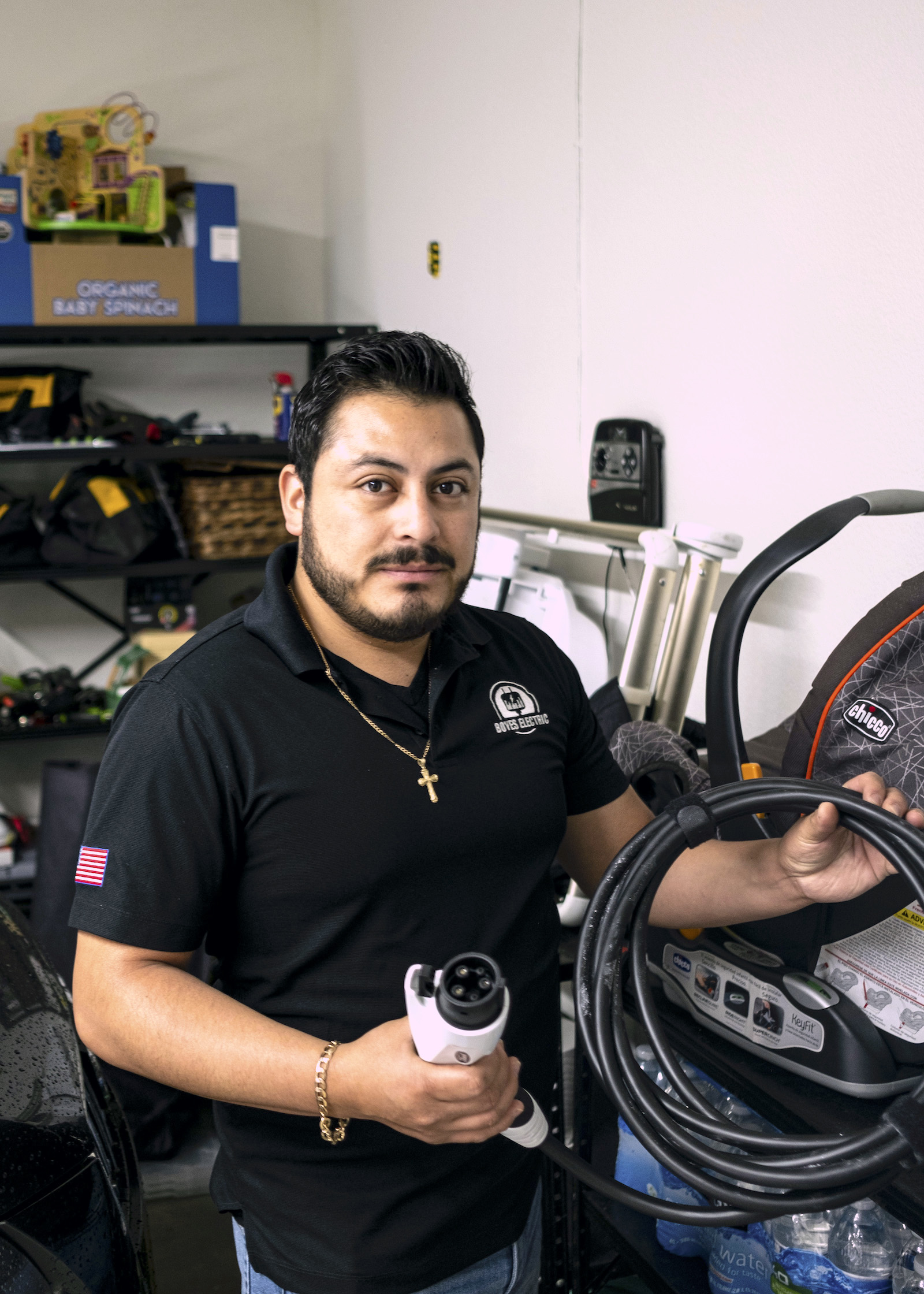 Un homme en chemise noire tient un chargeur de voiture dans un garage.