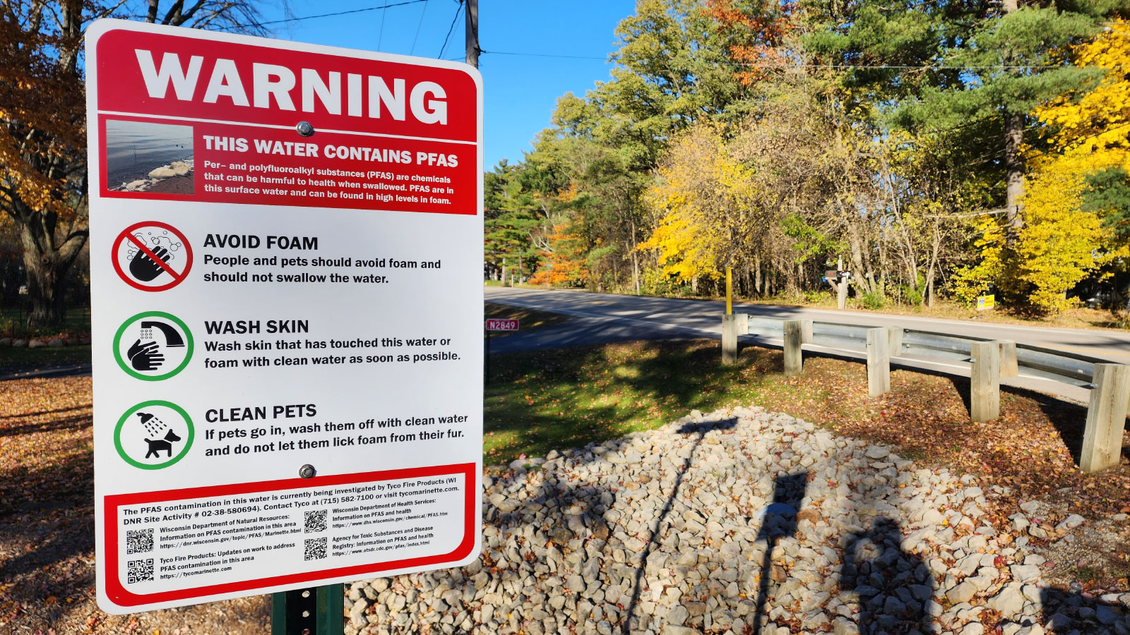 Panneau d'avertissement de PFAS dans l'eau avec des arbres d'automne et une route en arrière-plan