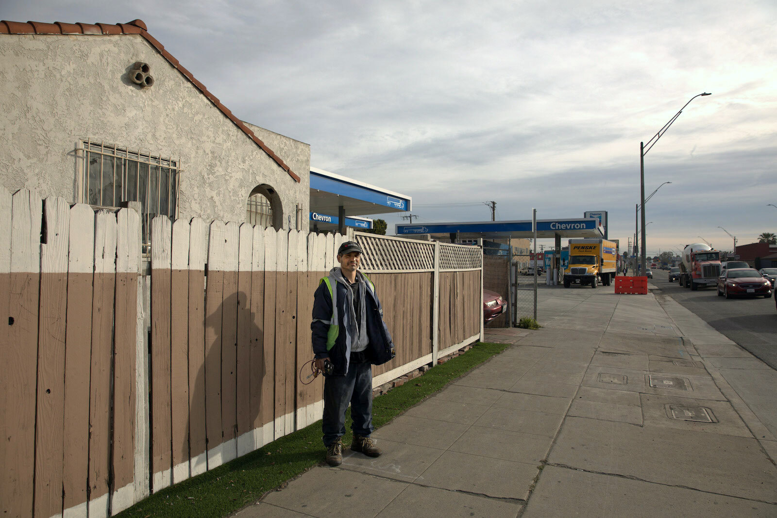 un homme se tient devant une clôture qui sépare une maison d'une station-service