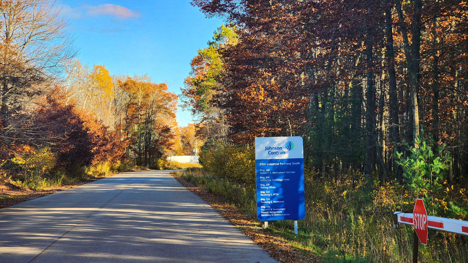 Route avec des arbres automnaux de chaque côté et un panneau indiquant l'installation de Johnson Controls
